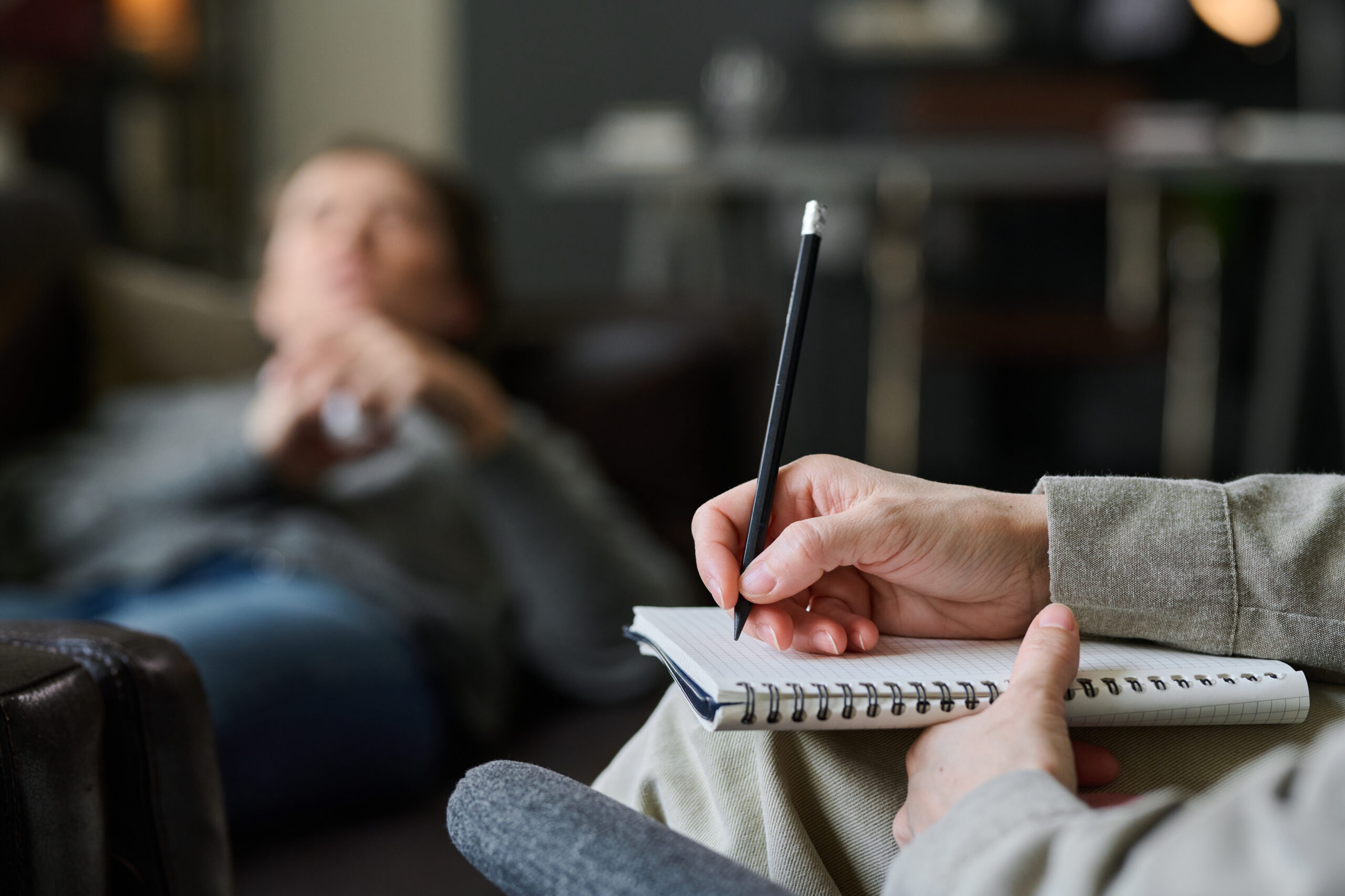 "Therapist holding pen and notepad during a confidential hypnotherapy session in La Jolla, CA, with a patient in the background."